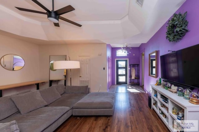 living area with visible vents, a tray ceiling, wood finished floors, and ceiling fan with notable chandelier