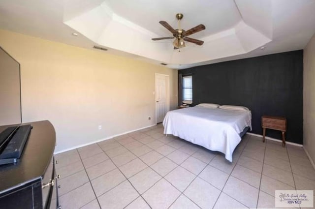 bedroom featuring light tile patterned flooring, a ceiling fan, visible vents, baseboards, and a tray ceiling