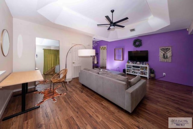 living area with visible vents, a tray ceiling, wood finished floors, and a ceiling fan