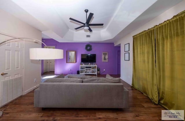 living area with ceiling fan, wood finished floors, visible vents, baseboards, and a raised ceiling