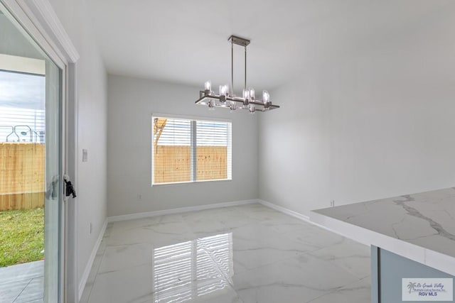 unfurnished dining area featuring baseboards, an inviting chandelier, and marble finish floor