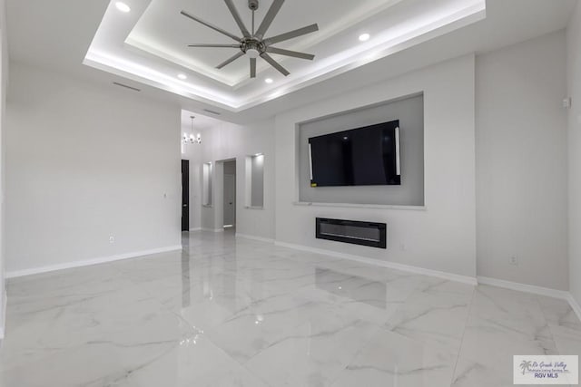 unfurnished living room featuring recessed lighting, baseboards, a raised ceiling, and ceiling fan with notable chandelier