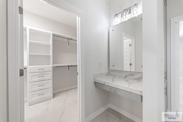 bathroom with baseboards, a walk in closet, and marble finish floor