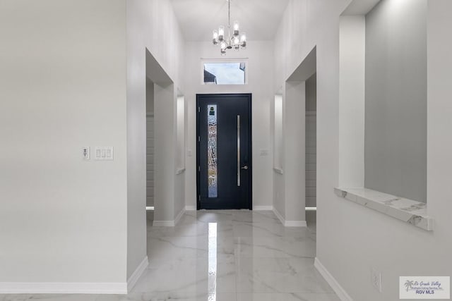 entryway with a high ceiling, marble finish floor, an inviting chandelier, and baseboards