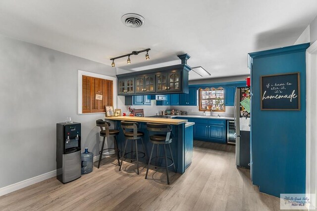 bar with blue cabinetry, light wood-type flooring, stainless steel refrigerator, and sink