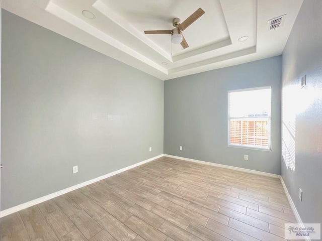 empty room featuring ceiling fan, light hardwood / wood-style floors, and a tray ceiling