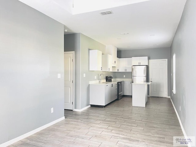 kitchen featuring sink, light hardwood / wood-style floors, appliances with stainless steel finishes, a kitchen island, and white cabinetry