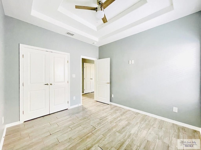 unfurnished bedroom featuring ceiling fan, a raised ceiling, and light wood-type flooring