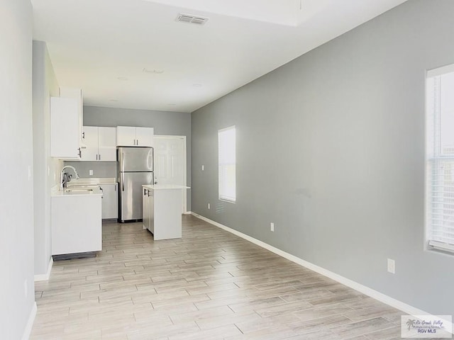 kitchen with white cabinetry, stainless steel fridge, sink, and light hardwood / wood-style floors