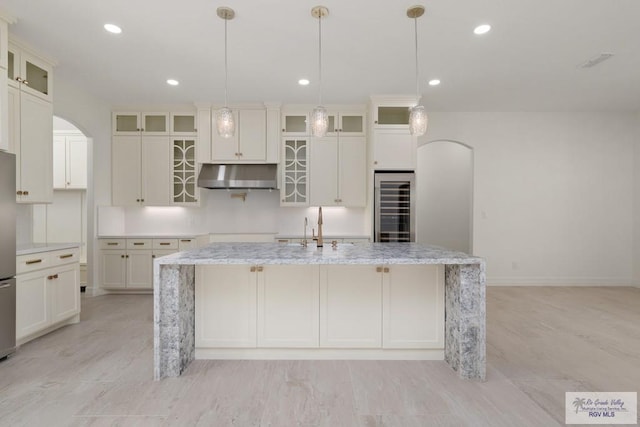 5407 Common Ln, Weslaco, TX 78596 - kitchen featuring beverage cooler, under cabinet range hood, a center island with sink, arched walkways, and light wood finished floors