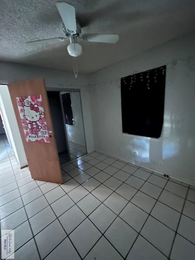 spare room featuring ceiling fan, light tile patterned floors, and a textured ceiling