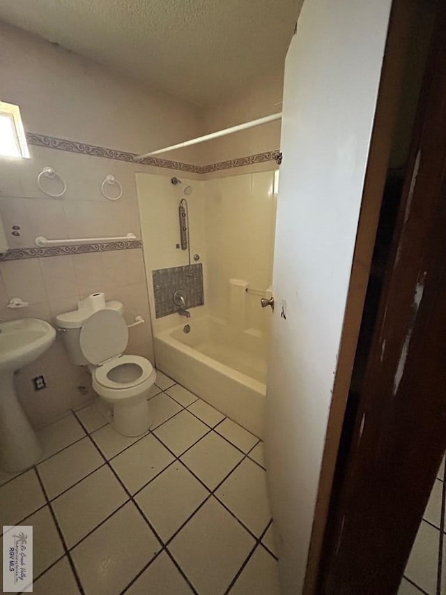 bathroom featuring tile patterned flooring, bathing tub / shower combination, a textured ceiling, toilet, and tile walls