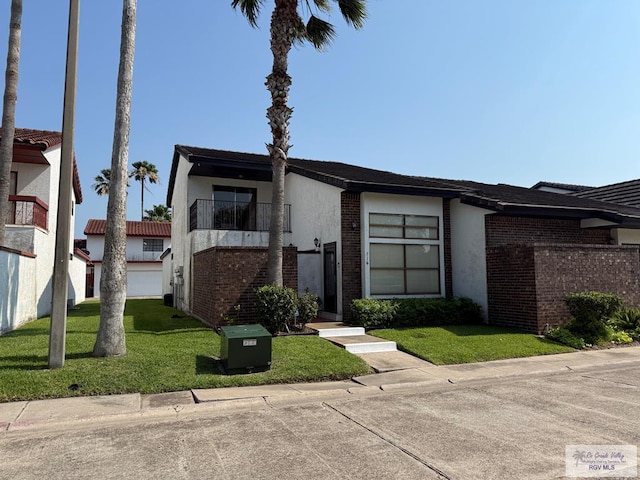 2100 W San Marcelo Blvd Unit 216, Brownsville, TX 78526 - view of front of property with stucco siding, a front lawn, a balcony, and brick siding