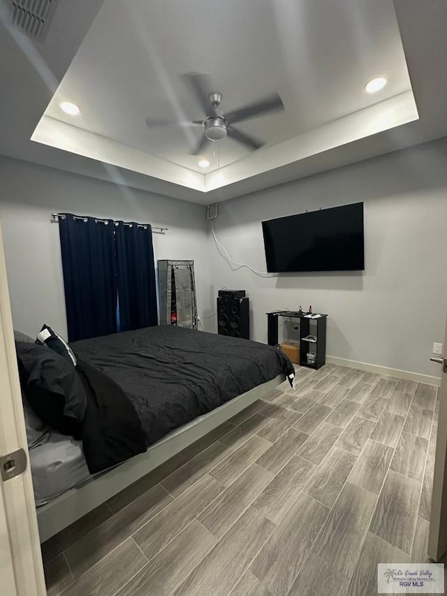 bedroom with ceiling fan, wood-type flooring, and a tray ceiling