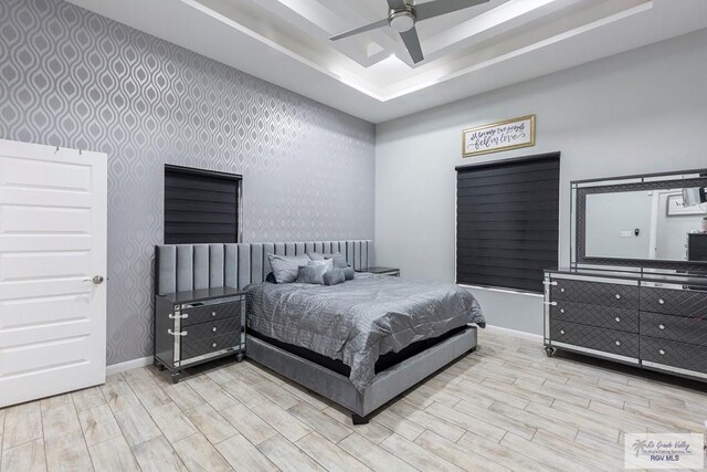 bedroom featuring ceiling fan, light wood-type flooring, and a tray ceiling