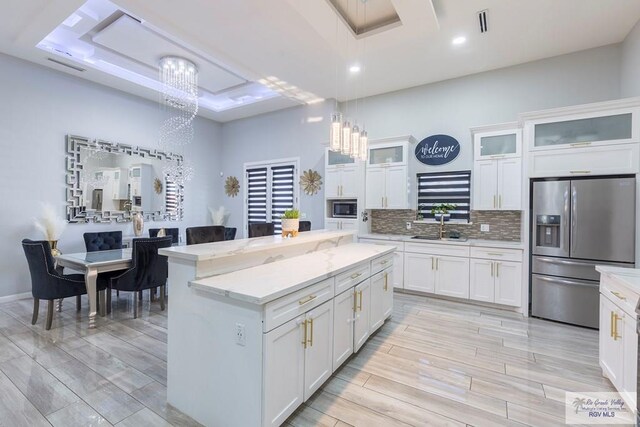 kitchen with appliances with stainless steel finishes, a raised ceiling, white cabinets, a center island, and hanging light fixtures