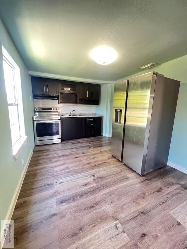 kitchen with tasteful backsplash, sink, appliances with stainless steel finishes, and light hardwood / wood-style flooring