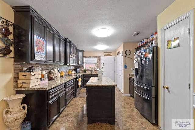 kitchen featuring backsplash, light stone counters, a textured ceiling, stainless steel appliances, and a center island