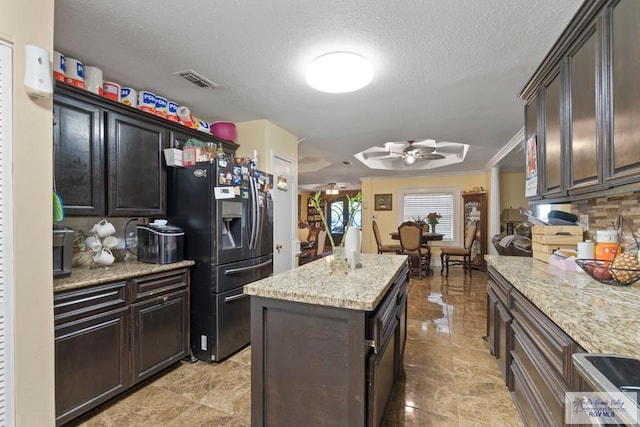 kitchen with stainless steel fridge, light stone counters, a textured ceiling, ceiling fan, and a center island