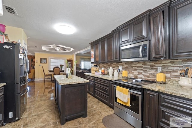 kitchen featuring backsplash, dark brown cabinets, stainless steel appliances, ceiling fan, and a kitchen island