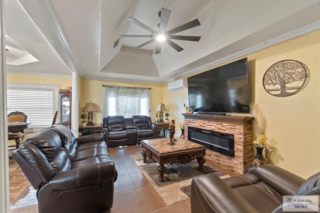 living room featuring a raised ceiling, a stone fireplace, tile patterned flooring, ceiling fan, and ornamental molding