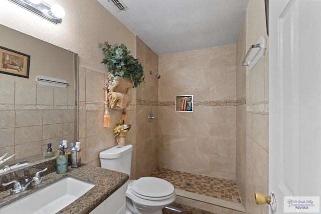 bathroom featuring tiled shower, toilet, tile walls, and vanity