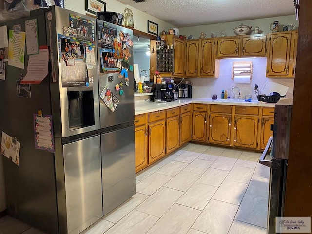 kitchen with a textured ceiling, stainless steel fridge, light tile patterned flooring, and sink