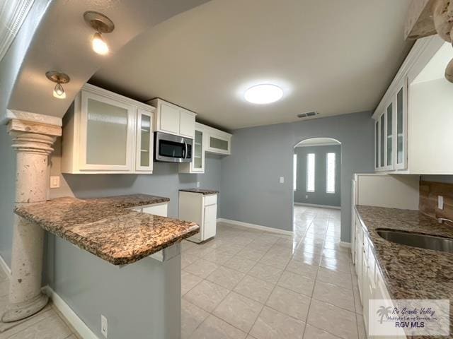 kitchen featuring kitchen peninsula, dark stone counters, sink, white cabinets, and light tile patterned flooring