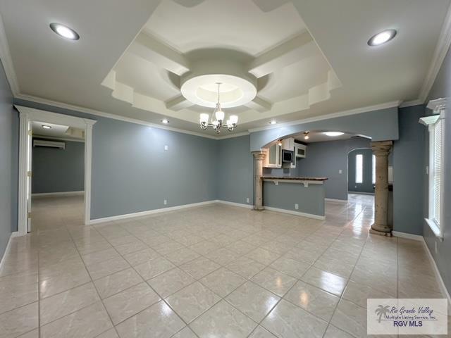 empty room featuring a tray ceiling, ornate columns, and ornamental molding