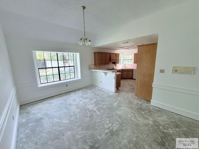 kitchen with sink, an inviting chandelier, kitchen peninsula, decorative light fixtures, and a textured ceiling