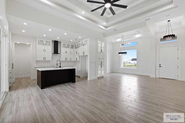 119 Finch Dr, Los Fresnos, TX 78566 - kitchen featuring wall chimney range hood, light countertops, ceiling fan with notable chandelier, a tray ceiling, and a center island with sink