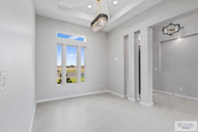 empty room featuring a raised ceiling and a chandelier