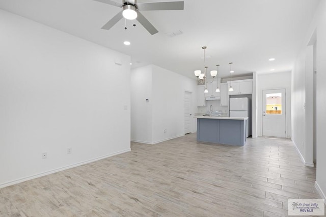 unfurnished living room featuring ceiling fan with notable chandelier, light wood-type flooring, and sink