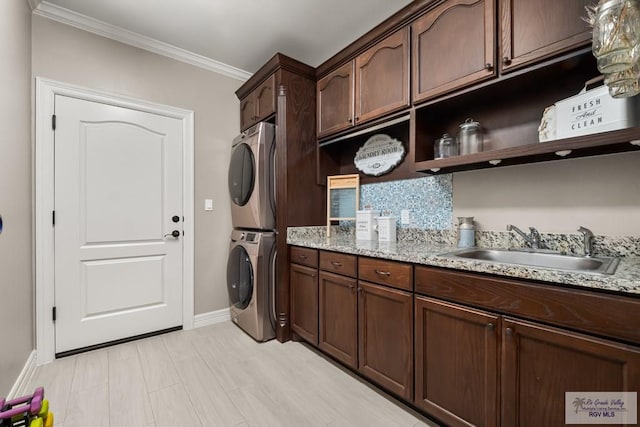 laundry room featuring crown molding, cabinets, stacked washer and clothes dryer, and sink