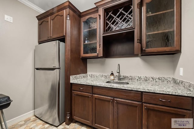 kitchen with sink, stainless steel fridge, dark brown cabinets, light stone countertops, and ornamental molding