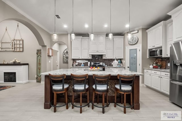 kitchen with white cabinetry, stainless steel appliances, hanging light fixtures, and a center island with sink