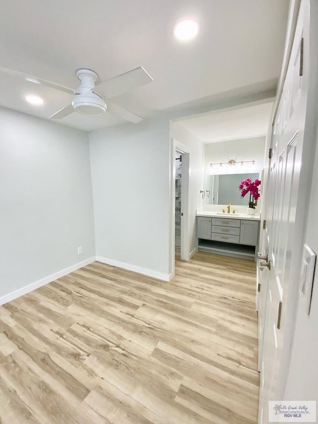 unfurnished bedroom featuring ceiling fan, a sink, baseboards, light wood finished floors, and ensuite bath