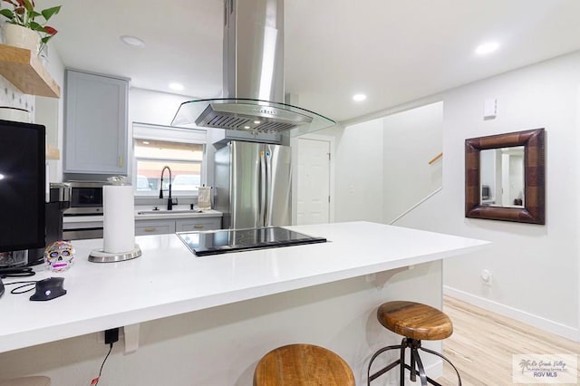 kitchen featuring gray cabinetry, sink, a kitchen bar, island range hood, and appliances with stainless steel finishes