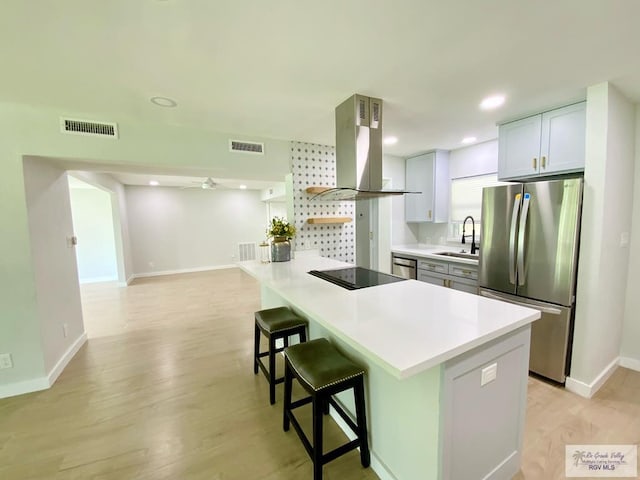 kitchen featuring exhaust hood, a breakfast bar area, visible vents, a sink, and freestanding refrigerator