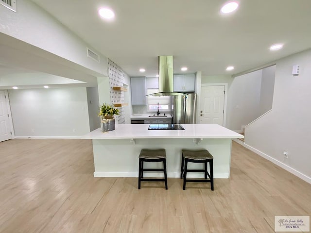 kitchen featuring light wood finished floors, light countertops, black electric cooktop, freestanding refrigerator, and island exhaust hood