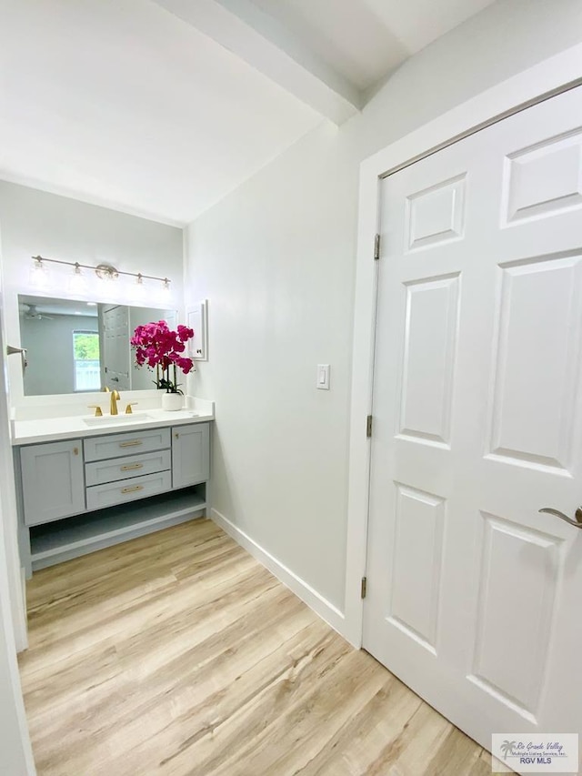 bathroom featuring vanity, baseboards, wood finished floors, and beam ceiling