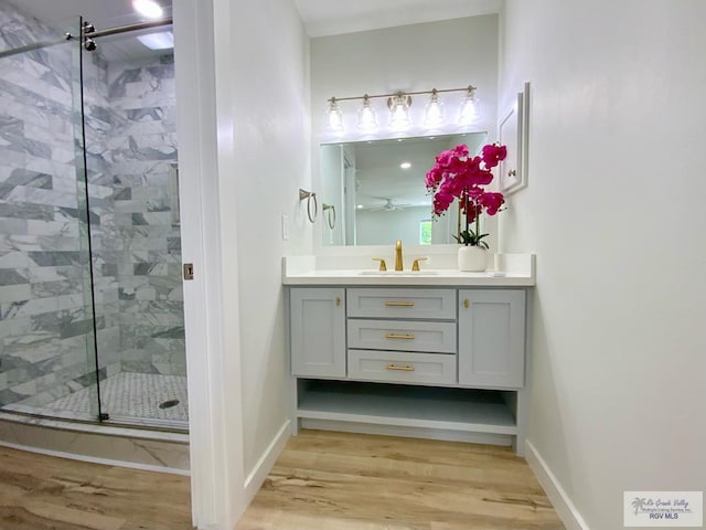 bathroom featuring wood finished floors, baseboards, a stall shower, and vanity