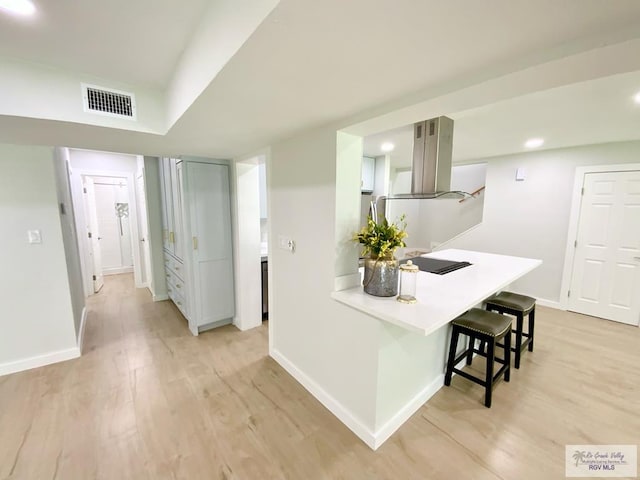 kitchen featuring a kitchen breakfast bar, visible vents, island range hood, baseboards, and light wood-style flooring