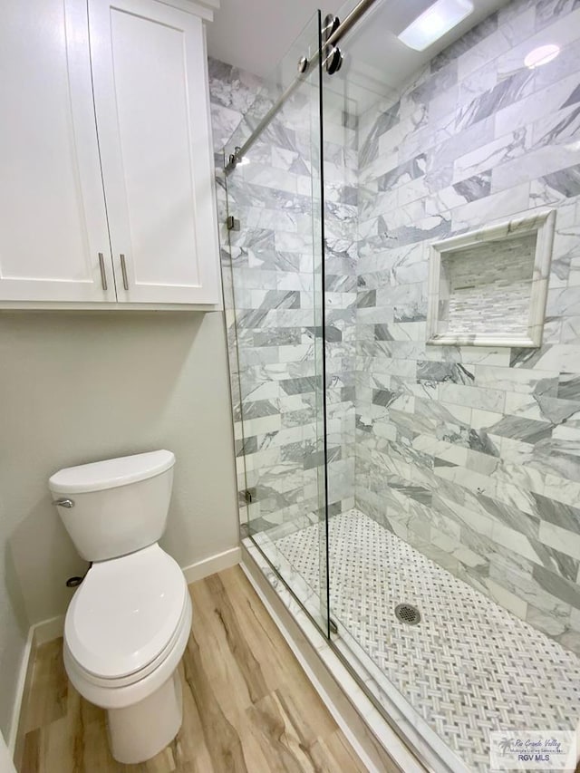 full bath featuring baseboards, a shower stall, toilet, and wood finished floors
