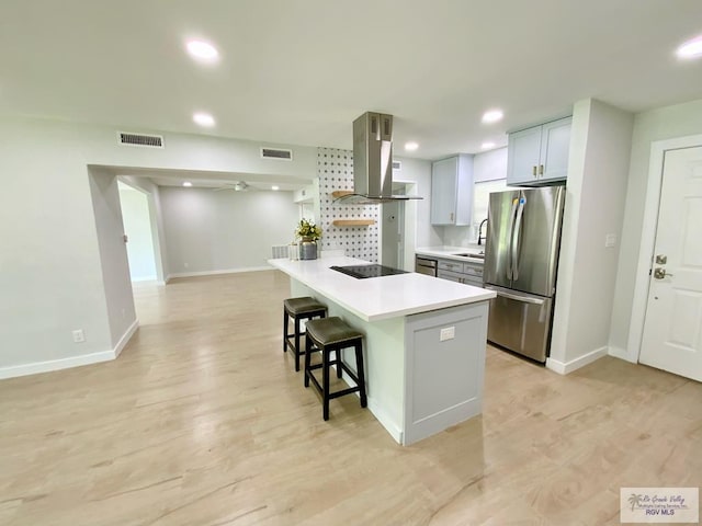 kitchen featuring black electric stovetop, a sink, freestanding refrigerator, island exhaust hood, and a kitchen bar
