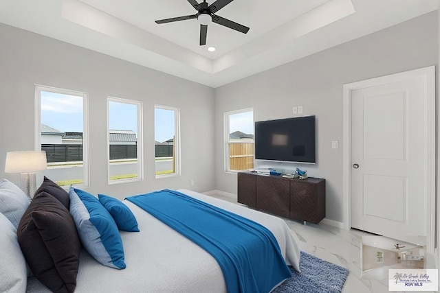 bedroom with multiple windows, ceiling fan, and a tray ceiling