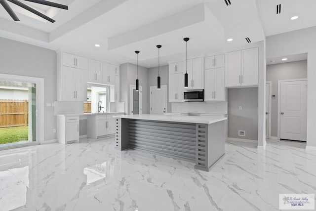 kitchen with hanging light fixtures, white cabinetry, a kitchen island, and a raised ceiling