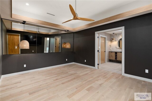 empty room featuring a raised ceiling, light hardwood / wood-style flooring, and ceiling fan