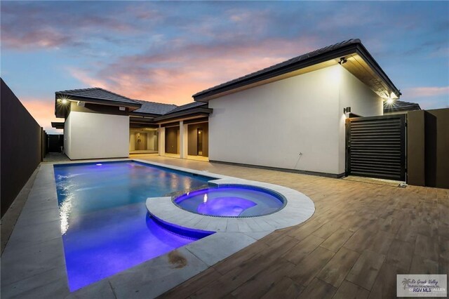 pool at dusk featuring an in ground hot tub