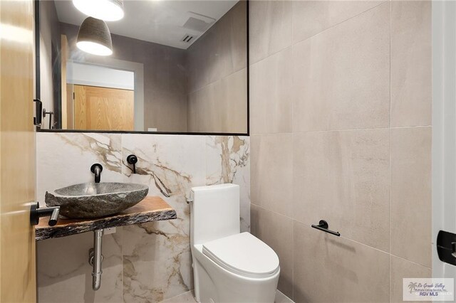 bathroom featuring backsplash, toilet, sink, and tile walls